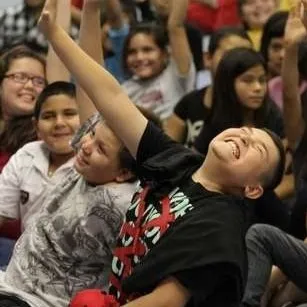 Excited students with hands raised participating in a school assembly show