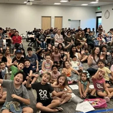 Large group of diverse children and parents sitting on the floor during an interactive school assembly program