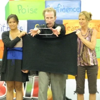 Performer holding a black cloth with two assistants in front of a colorful educational backdrop